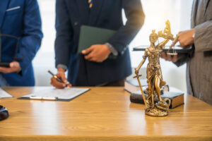 A team meeting of business people and a lawyer in formal suits is taking place at a desk, discussing a contract and various aspects of the law and litigation.